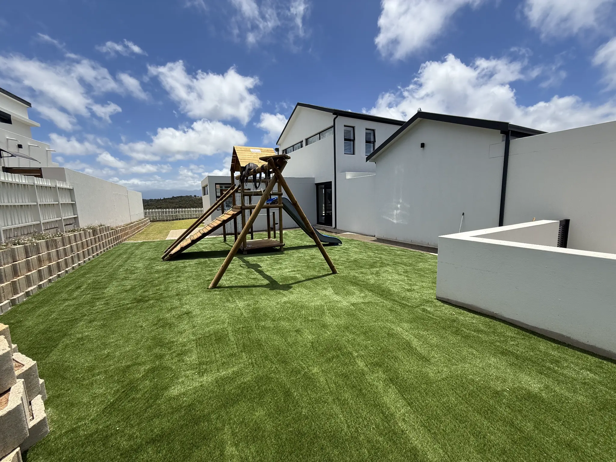 Artificial grass family play lawn with a timber play structure beside a modern home