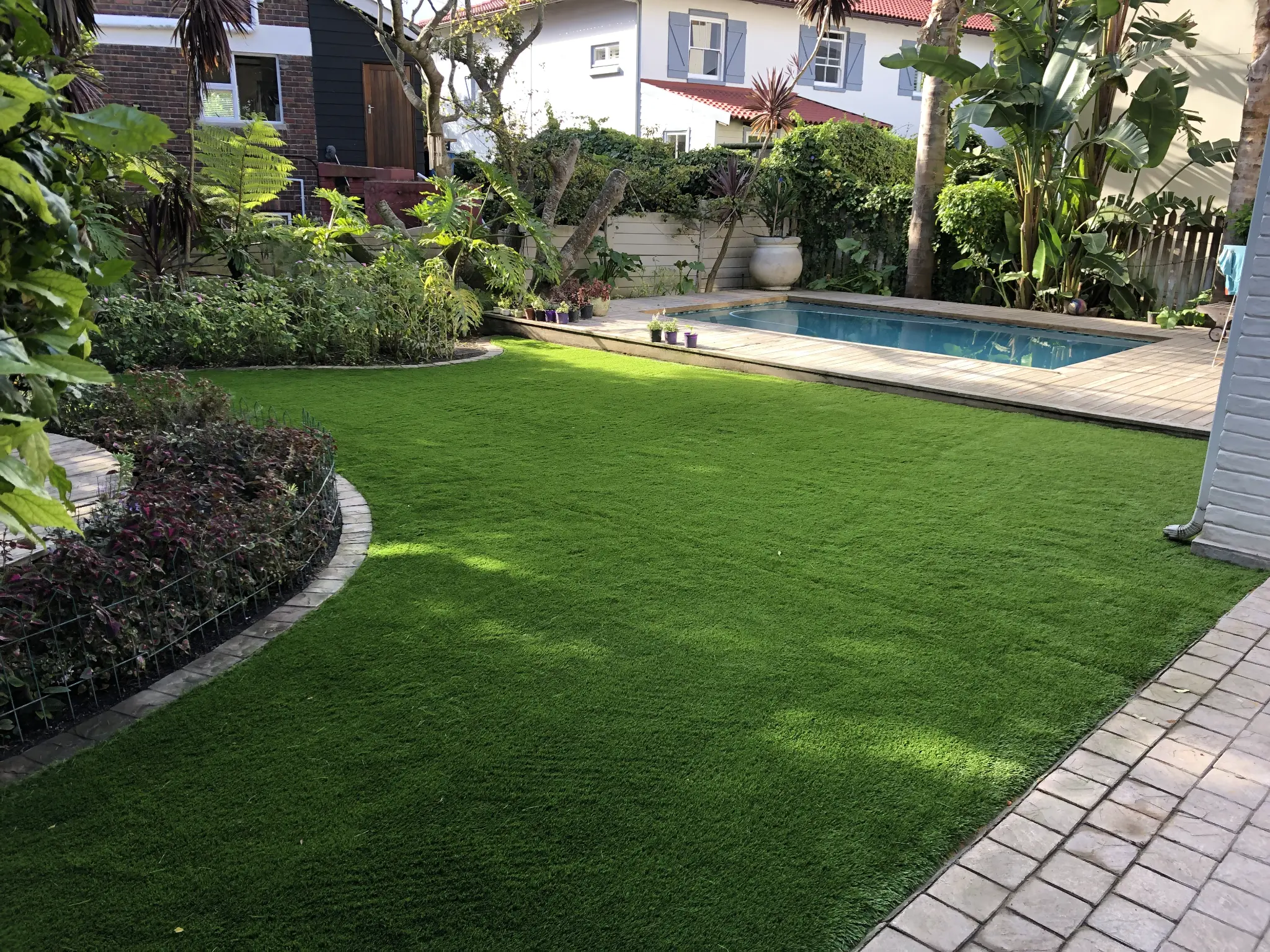 Artificial grass garden beside a pool with brick paving and planted beds