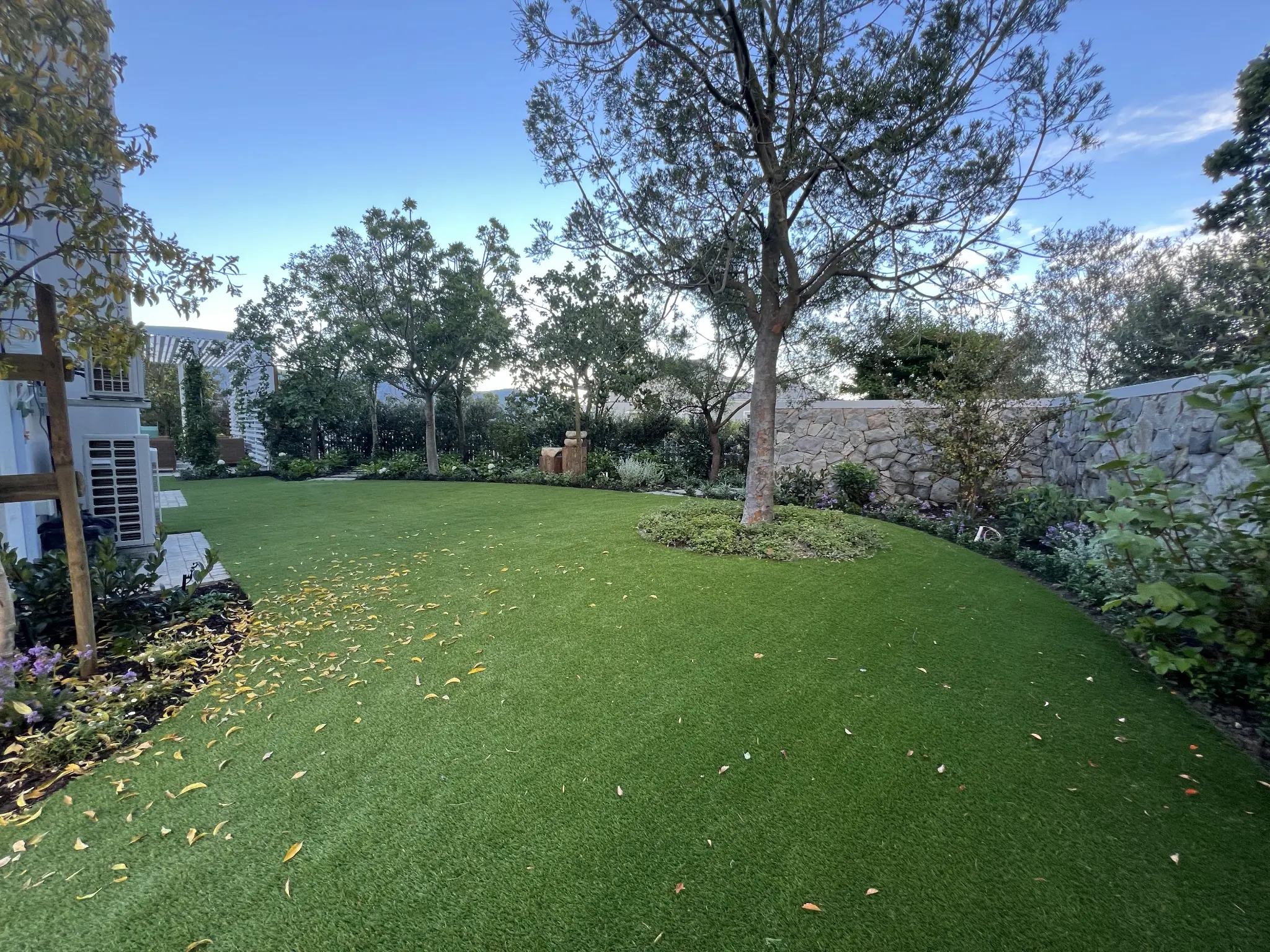 Artificial grass lawn set within mature trees, planted borders and a stone garden wall