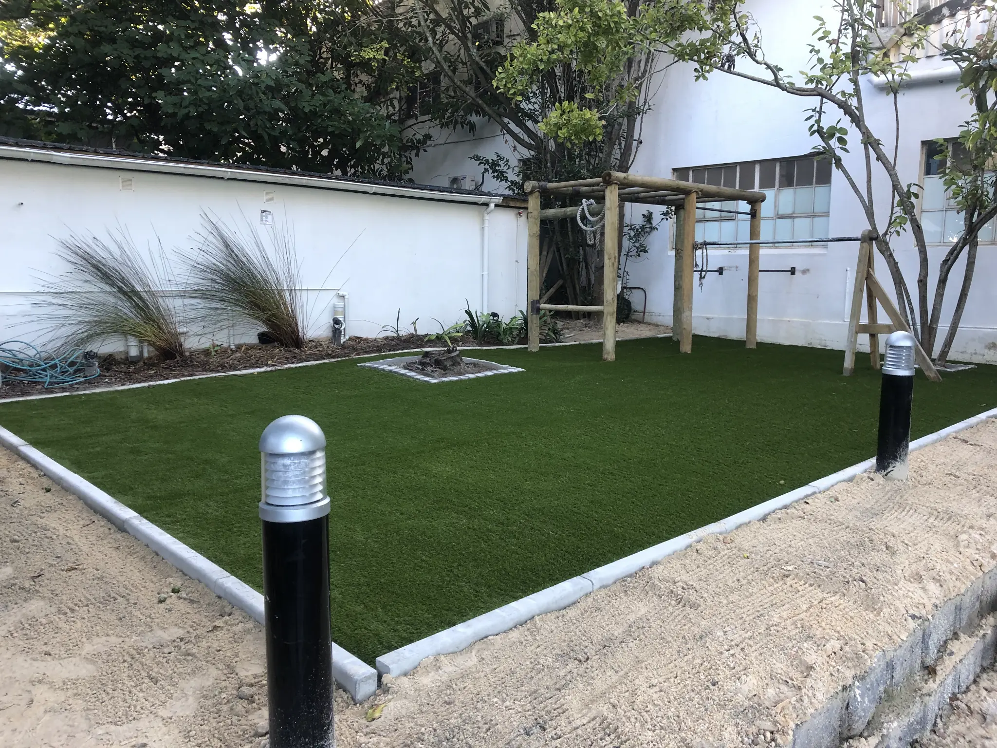 Artificial grass courtyard play area with timber climbing frame and planted edges